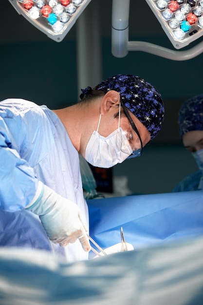 Een gespannen professionele chirurg naait een wond dicht in de operatiekamer een modern medisch licht schijnt op hem een rustige mannelijke chirurg copyspace
