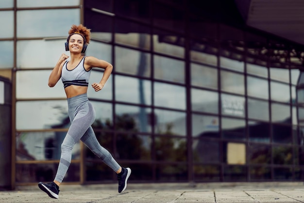 Een gespierd jong meisje in sportkleding is aan het joggen in een stadswijk terwijl ze naar haar favoriete muziek luistert. Geen excuses, alleen goede wil en moeite