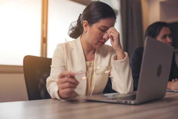 Een gestresste vrouw zit aan haar bureau op kantoor Na een lange periode van laptopgebruik zet een vermoeide zakenvrouw haar bril af die lijdt aan vermoeide ogen en droge ogen-syndroom