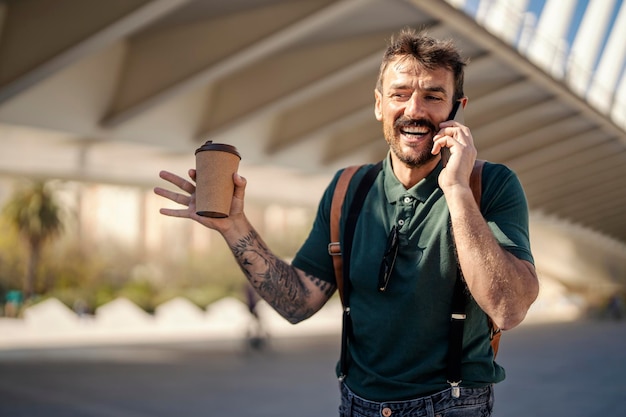 Een getatoeëerde retro man drinkt zijn koffie terwijl hij aan het telefoneren is op straat in de stad