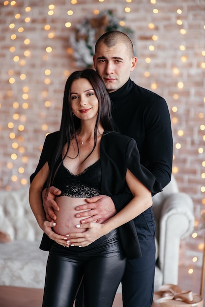 Een getrouwd stel, een man en een zwangere vrouw poseren tegen de achtergrond van een grijze locatie