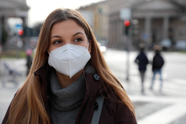 Een gevoel van verbijstering. Sluit omhoog van jonge vrouw die in de winterkleren in straat loopt die beschermend masker FFP2 KN95 draagt. Meisje met gezichtsmasker voelt zich alleen tijdens een pandemie.