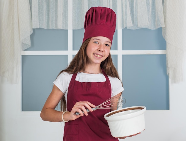 Een geweldige ervaring kind koken eten in de keuken een carrière kiezen kleine helper gebruik klopper culinaire en keuken gelukkige jeugd gelukkig kind dragen kok uniform chef-kok meisje in hoed en schort