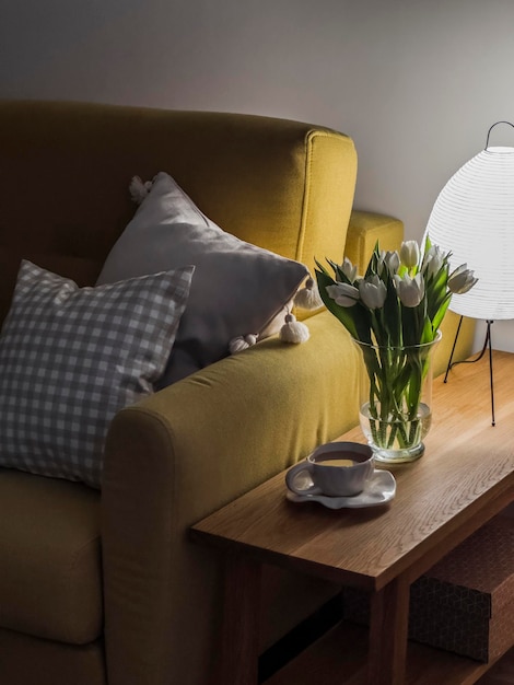 Een gezellige thuis avond een kop thee een boeket witte tulpen in een glazen vaas een lamp op een houten bankje naast een fauteuil