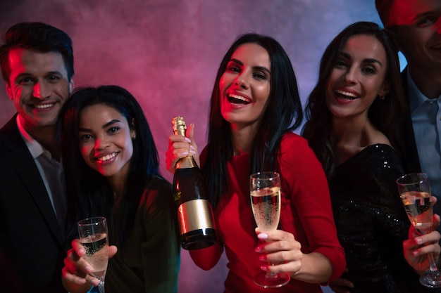Een gezelschap van vijf jonge en aantrekkelijke mensen viert feest, geniet van elkaars gezelschap, drinkt champagne en poseert samen met fluiten