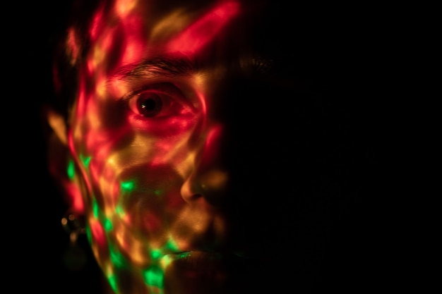 een gezicht in het donker bedekt met felgekleurde vlekken van een felle lamp gekleurde schittering van de lamp