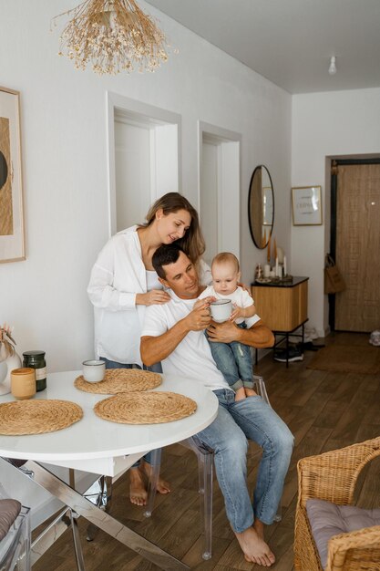 Een gezin van drie is aan het ontbijten mama staat koffie te drinken papa en baby