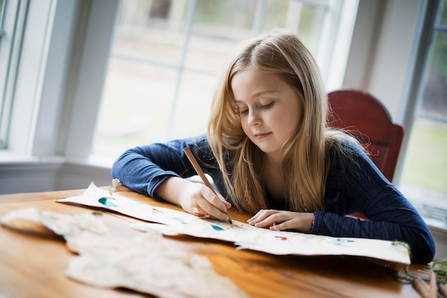 Een gezinswoning een jong meisje dat aan een tafel zit te tekenen op een groot stuk papier een potlood in de hand houden