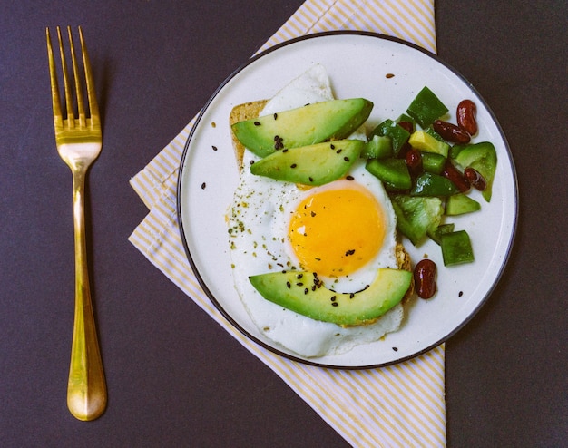 Een gezond ontbijt van toast met avocado, volkoren brood en gebakken ei en burrito salade op een witte plaat. Bovenaanzicht