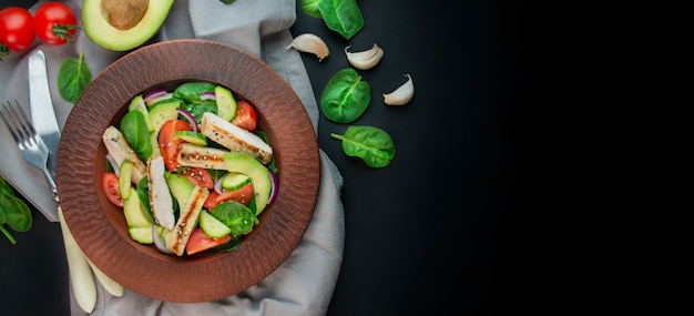 Een gezonde salade van kipfilet, verse groenten, spinazie, avocado en tomaten op een donkere achtergrond. salade van groenen met vlees. het concept van dieetvoeding. kopieer ruimte. benner eten.