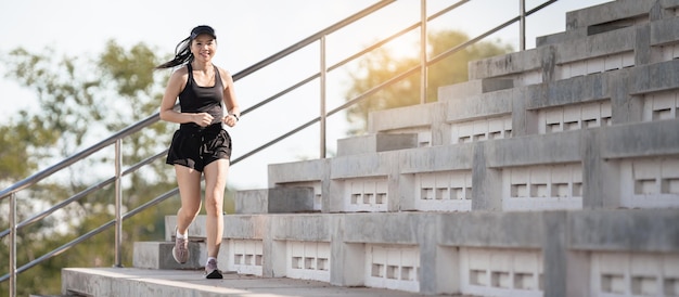 Een gezonde volwassen Aziatische vrouw rent op betonnen trappen van het stadsstadion om het lichaam te versterken
