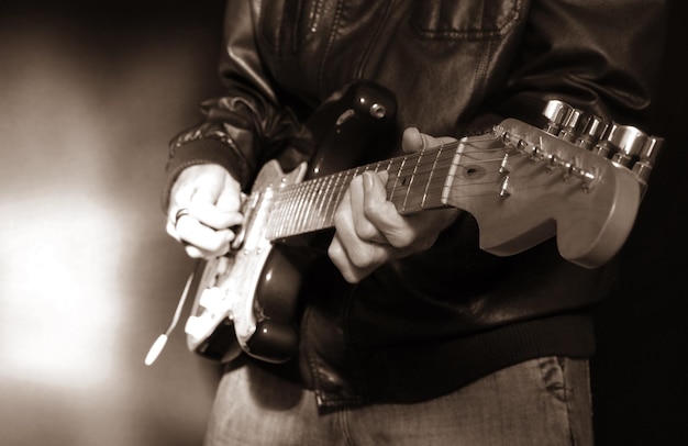 Foto een gitarist in een lederen jas die een elektrische gitaar met vijf snaren speelt