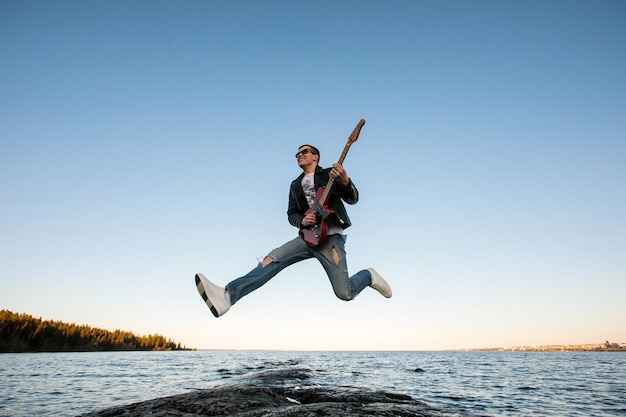 Een gitarist speelt een elektrische gitaar in een sprong tegen de achtergrond van een vijver en blauwe lucht