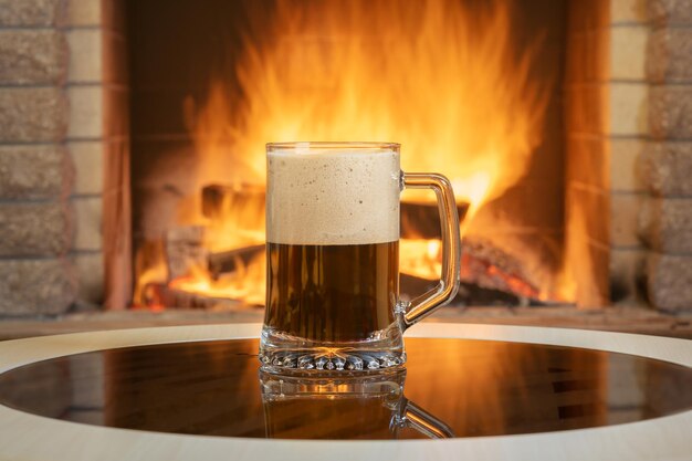 Een glas bier met schuim in de buurt van gezellige open haard brandende achtergrond.