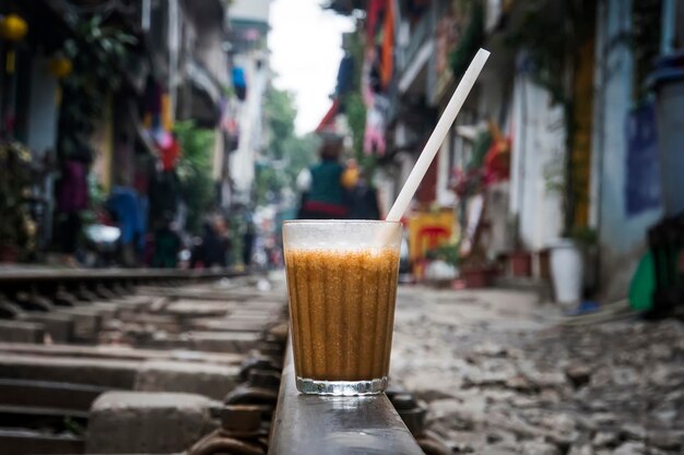 Een glas bruine koude koffie staat op het spoor in Hanoi, Vietnam Een van de attracties van Hanoi, een trein die tussen de oude huizen doorgaat in een smalle stadsstraat