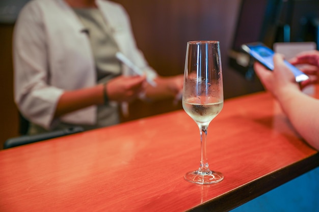 Een glas champagne staat op een toog met een persoon die een telefoon vasthoudt.