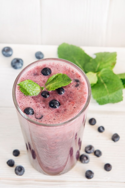 Een glas gezonde bosbessen en bananen smoothie op witte houten achtergrond versierd met munt.