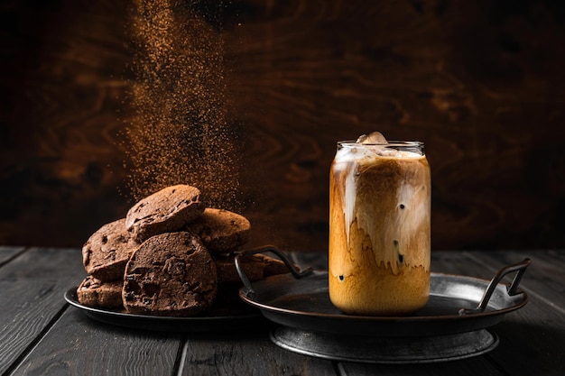 Een glas ijskoffie met melk en chocoladekoekjes op een bord, cacaopoeder valt