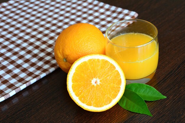 Een glas jus d'orange naast een groep sinaasappelfruit en geruit tafelkleed