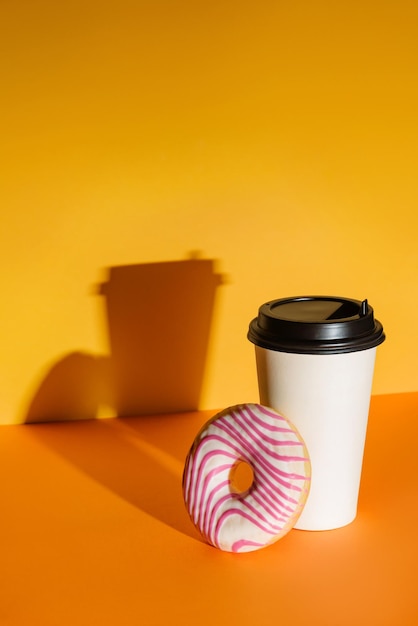 Een glas koffie en een geglazuurde donut op een fel oranje en gele achtergrond.