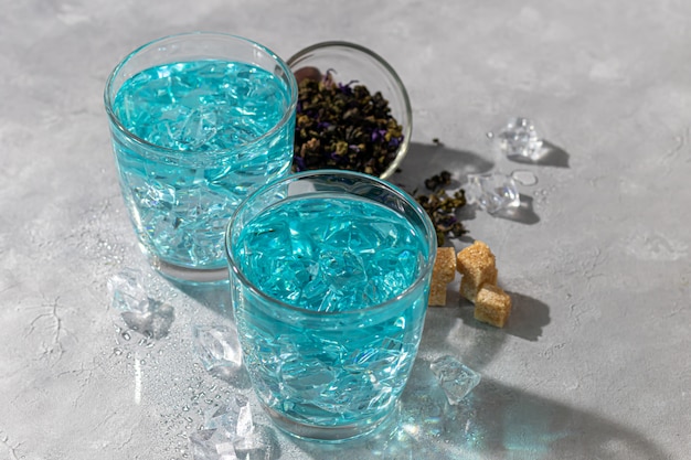 Een glas koude, blauwe thee met erwtenbloemen en ijs. Blauwe erwten. Voor gezond drinken, het lichaam ontgiften. Grijze tafel.