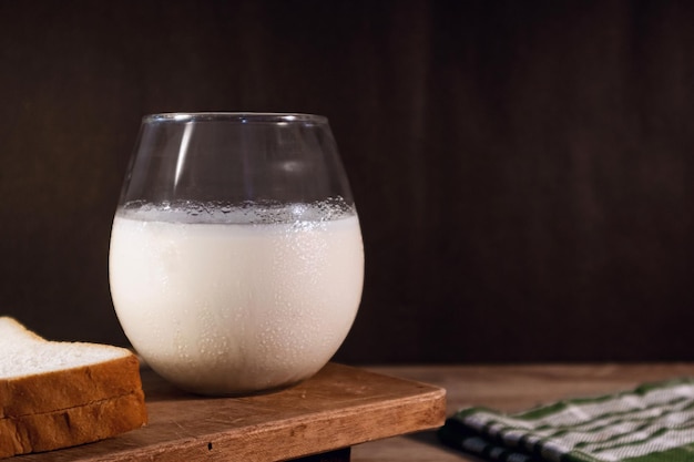 Een glas koude melk en wit brood op een houten tafel op een donkere achtergrond