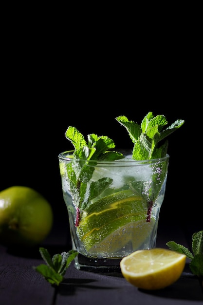 Een glas koude mojito met limoen, citroen en munt op een zwarte houten achtergrond Close-up van een verfrissende cocktail