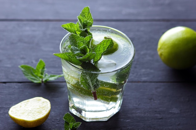 Een glas koude mojito met limoen, citroen en munt op een zwarte houten achtergrond close-up van een verfrissende cocktail