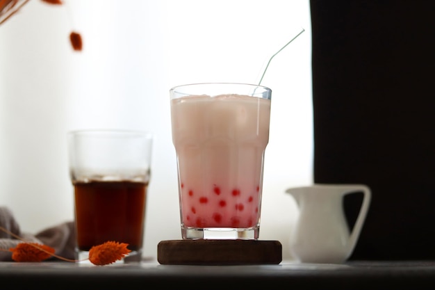 Een glas melk met een rietje en een kopje thee op tafel.