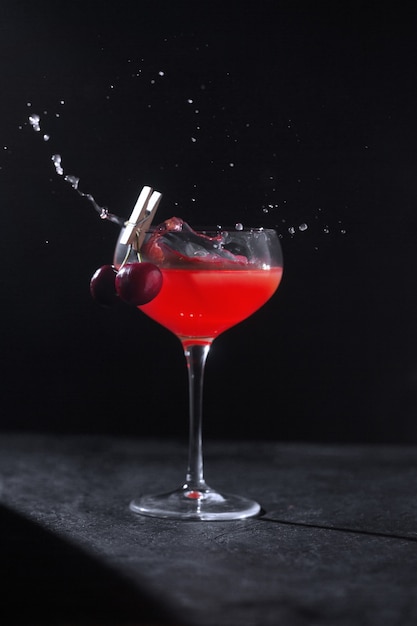 Een glas met een gekoelde alcoholische cocktail gemaakt door een barman versierd met kersen op een wasknijper en spatten. Laagdrempelig
