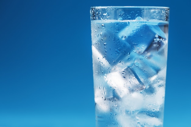 Een glas met ijswater en ijsblokjes op een blauwe ondergrond