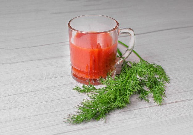 Een glas met tomatensap en een groene sig van dille op tafel