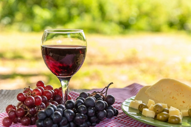 Een glas rode wijn en een bord kaas, olijven en druiven op tafel.