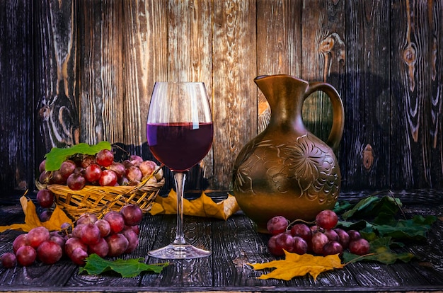 Een glas rode wijn en een kruik druiven op een tafel.
