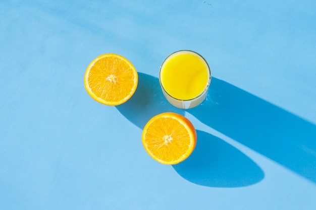 Een glas sinaasappelsap en sinaasappelen op een blauwe achtergrond. Tropisch concept van vitaminen, zomer. Natuurlijk licht. Plat lag, bovenaanzicht.