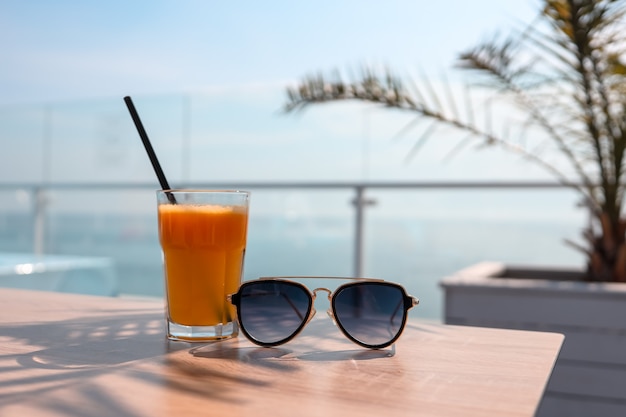 Een glas sinaasappelsap en zonnebril op de achtergrond van de zee.