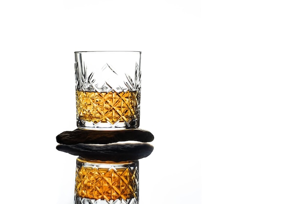 Een glas transparante whisky staat op een platte steen met een reflectie op een witte achtergrond