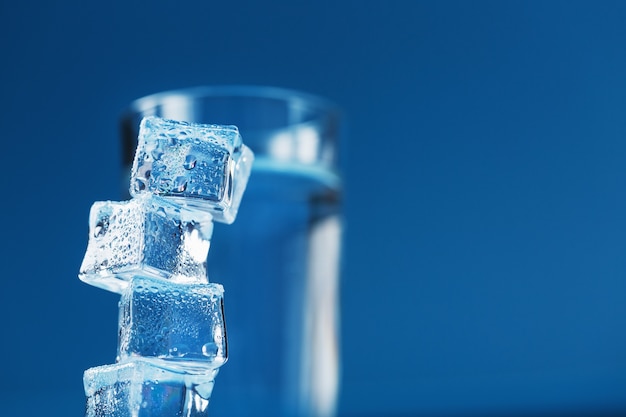 Een glas verfrissend water en een toren van ijsblokjes op een blauwe achtergrond