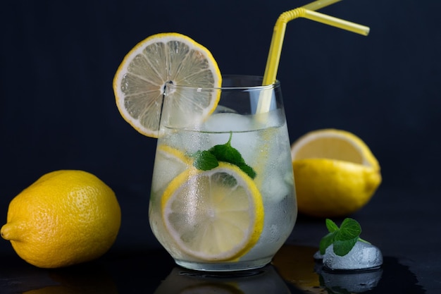 Een glas verfrissende zomeralcoholische cocktail Mojito-limonade met citroenmunt en gemalen ijs close-up gele rietjes