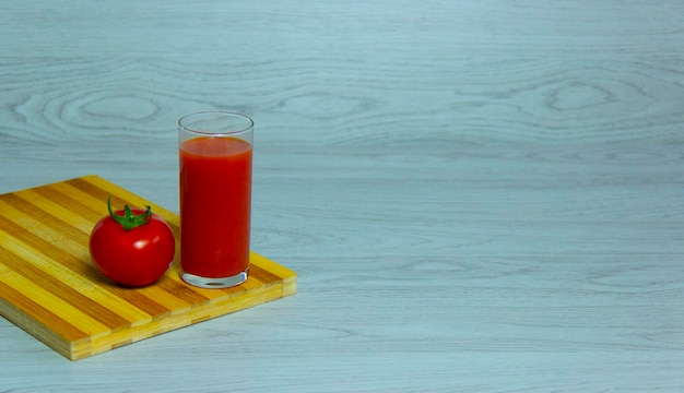 Foto een glas vers tomatensap en rode tomaten op een houten plank