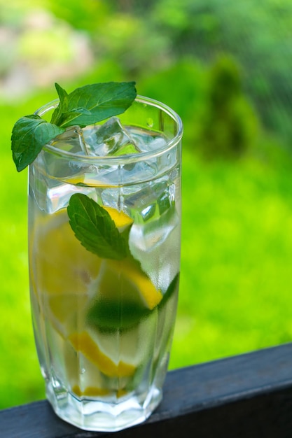 Een glas water met citroen en munt op de achtergrond van vers zomergroen gras Verkoelend drankje