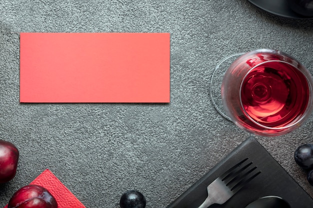 Een glas wijn en een rode ansichtkaart op een grijze betonnen tafel een uitnodiging voor een cele...