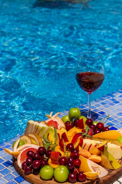 Een glas wijn met fruitplakken staat bij het zwembad