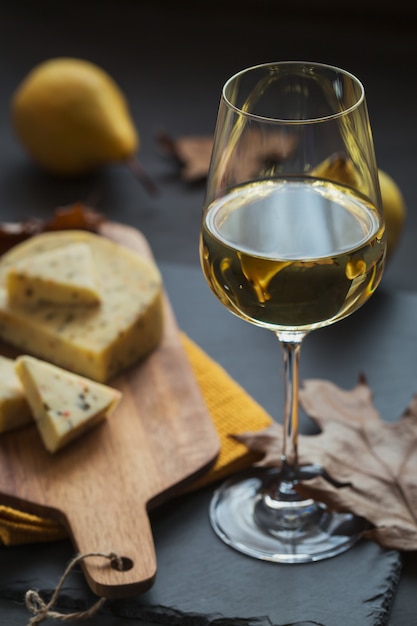 Een glas witte wijn geserveerd met kaas in een snijplank op donkere achtergrond