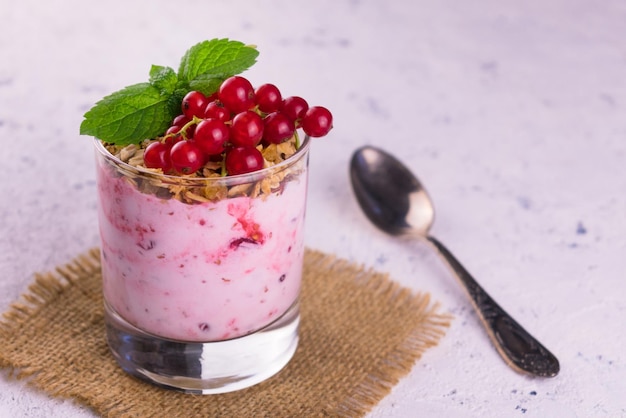 Een glas yoghurt met granola en rode aalbesbessen op een witte achtergrond