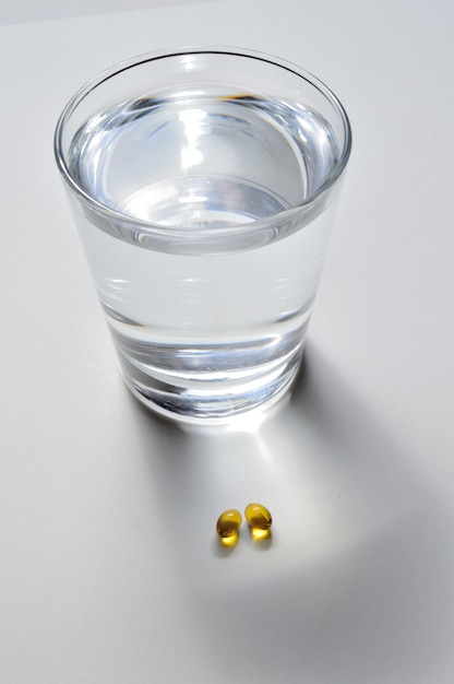 Een glazen beker en twee gele tabletten met vitamines. detailopname.