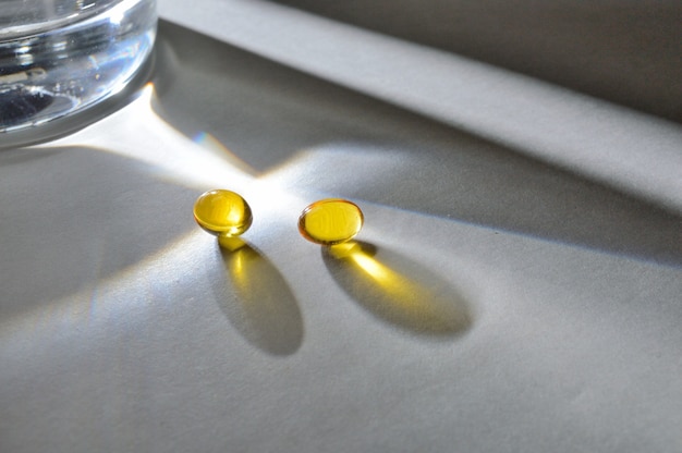 Een glazen beker en twee gele tabletten met vitamines. detailopname.