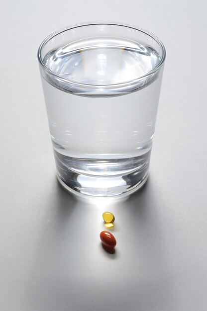 Een glazen beker en twee gele tabletten met vitamines. detailopname.