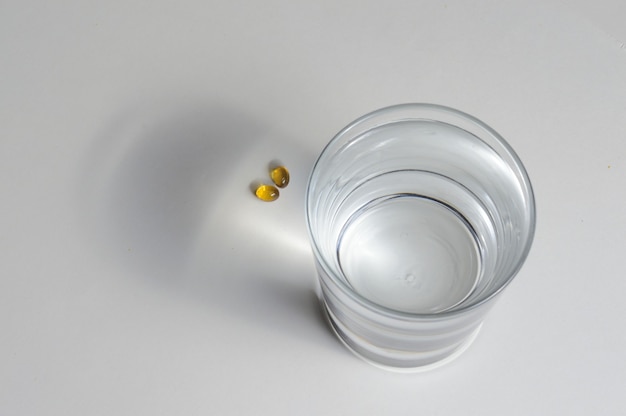 Een glazen beker en twee gele tabletten met vitamines. detailopname.