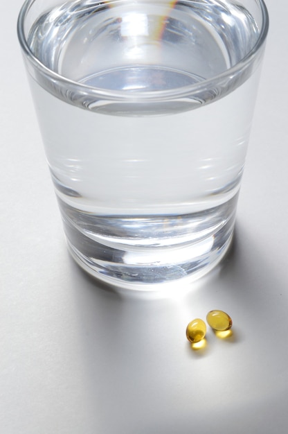 Een glazen beker en twee gele tabletten met vitamines. detailopname.